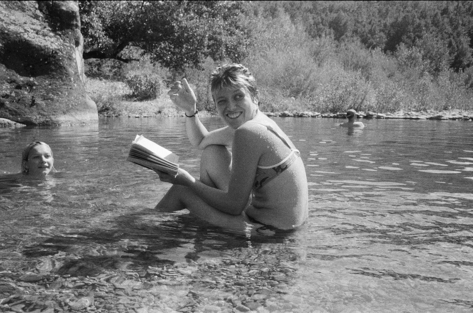 Black and white photograph of a woman reading a book while sitting in a river