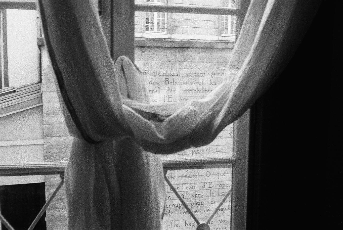 Black and white photograph looking through a window with curtains